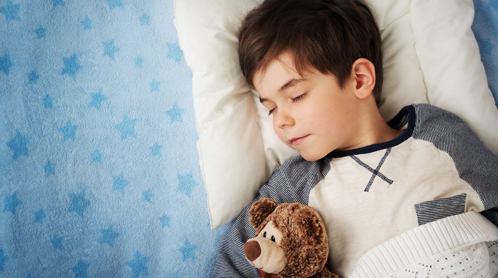 young boy holding stuffed teddy bear while sleeping in bed